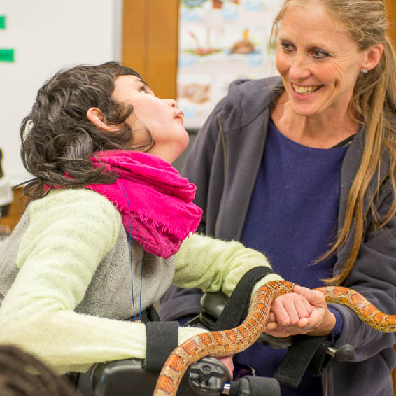 Student using assistive device holds a snake while adult looks on and smiles
