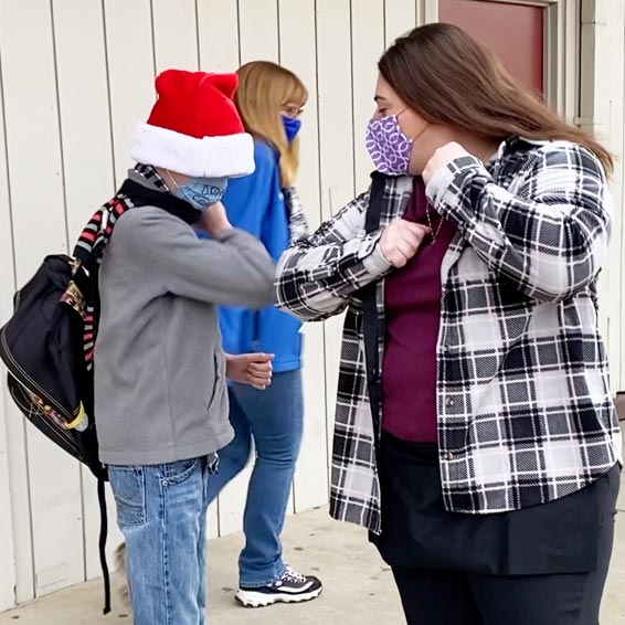 Teacher and student bumping elbows outside a classroom.