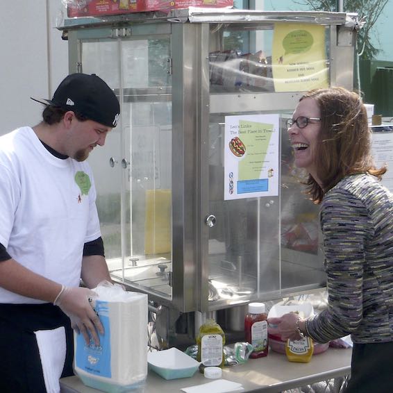 Staff purchasing hot dogs from student at cart