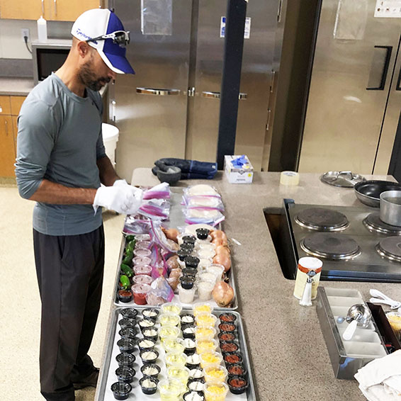 Staff member wearing gloves packaging trays of ingredients for student meal kits