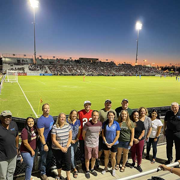 Group of teachers and classified staff posing in front of soccer pitch
