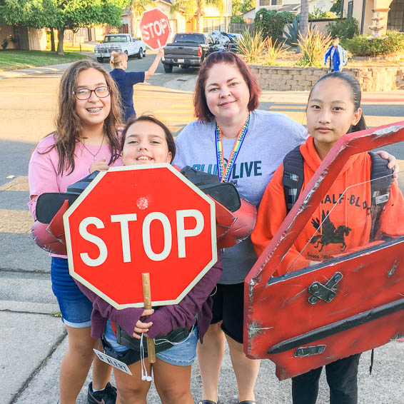 Students on sidewalk holding a car door and a stop sign