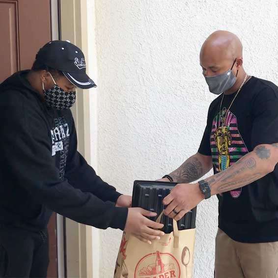 Teacher hands bag of planting supplies to student at his home