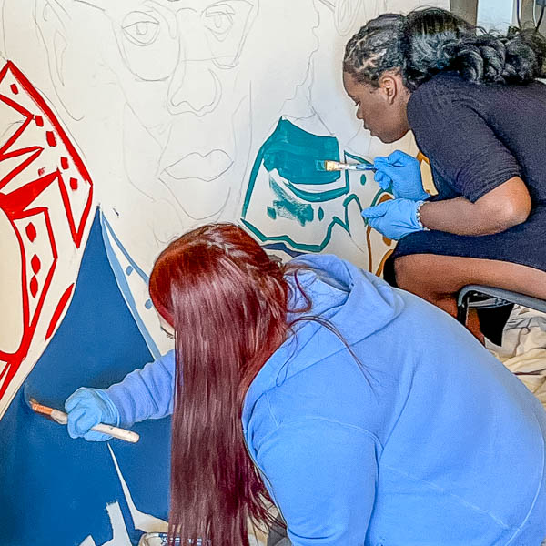 Students painting inside outlines of mural