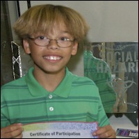 Student holding certificate of participation, standing in front of his artwork