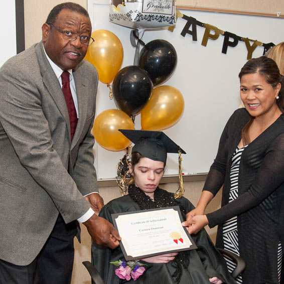 Alfred Brown and parent present certificate to seated student wearing cap and gown