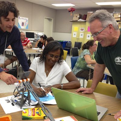 Teachers gathered around science equipment and a MacBook Pro