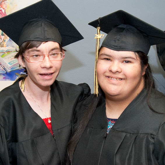 Students wearing black caps and gowns pose side by side and smile