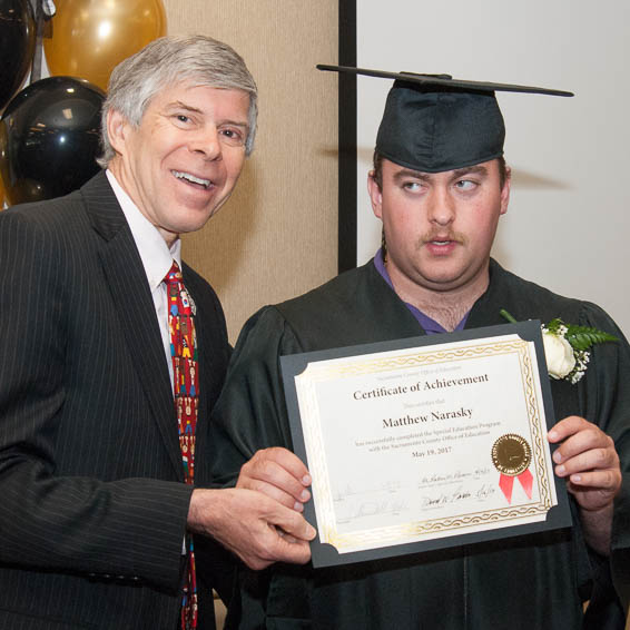 Greg Geeting presents certificate to seated student wearing cap and gown