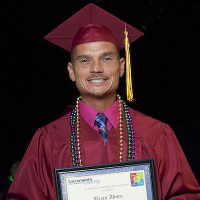 Client in maroon cap and gown holding certificate