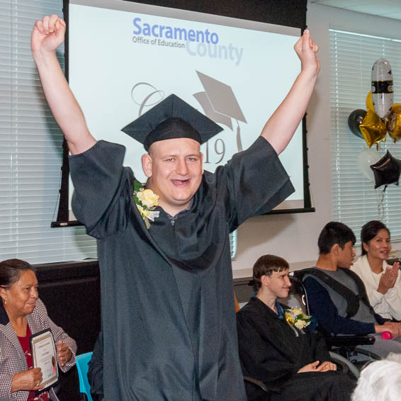 Student wearing graduation robe cheering with raised arms