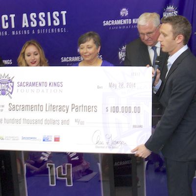 Kings representative holding large check showing $100,000 total donation.