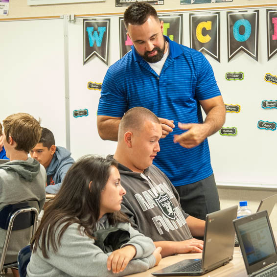 Teacher helping students with work on laptops