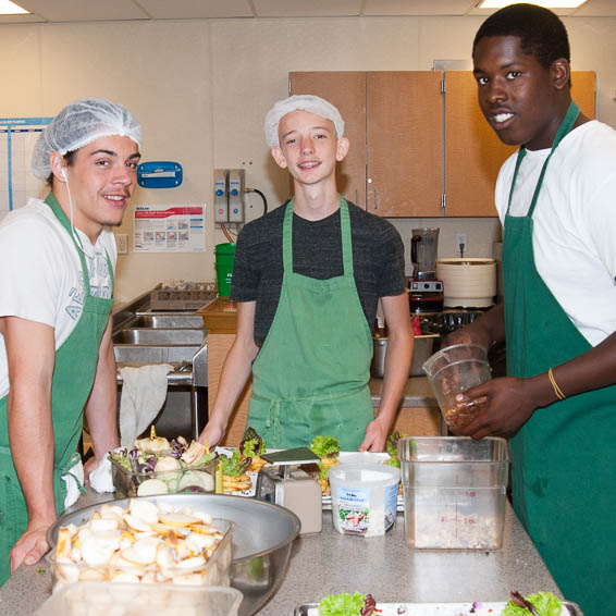 Students wearing green aprons prepare food