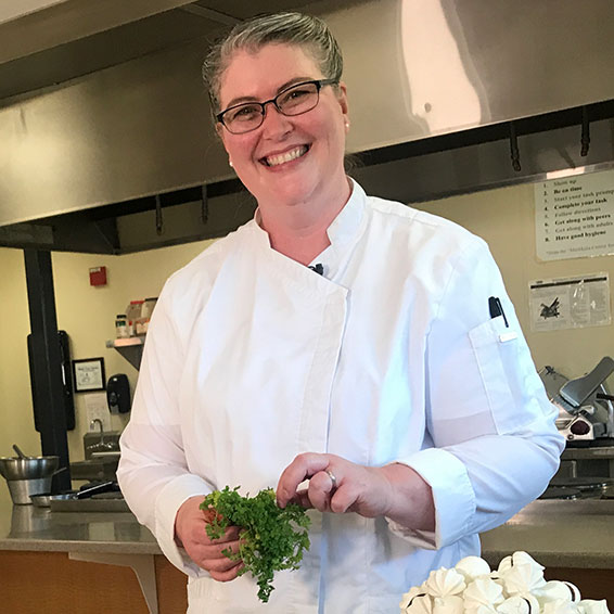 Carissa Jones wearing white chef's jacket and holding a bunch of herbs
