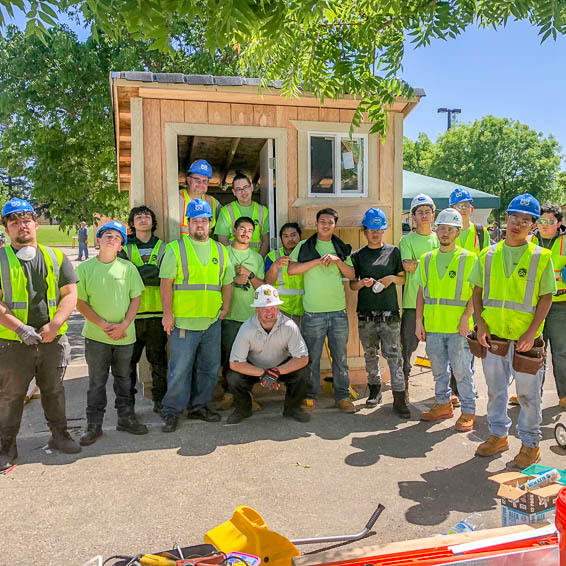 Students wearing construction gear and posing in front of shed