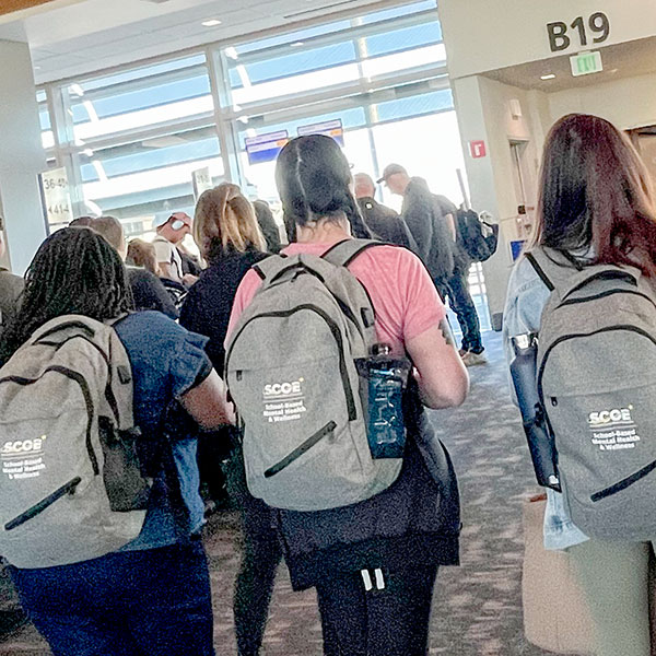 Clinicians walking to boarding gate with custom SCOE SBMHW program backpacks