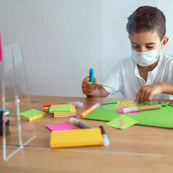 Student wearing a mask as he works behind plexiglass