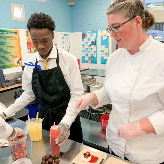 Teacher helping student prepare salad