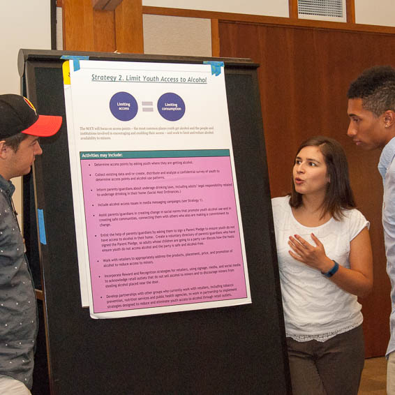 Students standing next to large display board presenting steps of plan