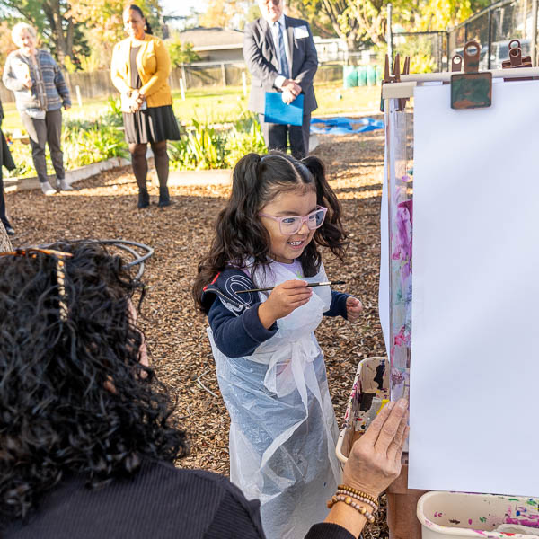 Student painting outside with visitors looking on