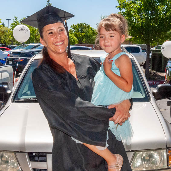 Certificate recipient holding daughter, standing in front of donated vehicle