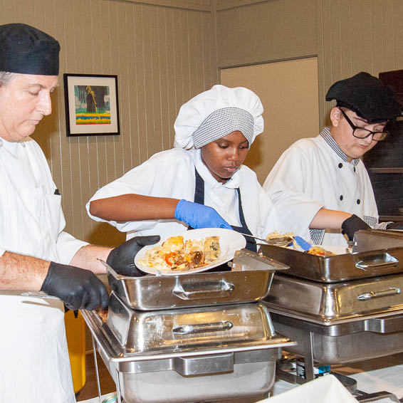 Instructor helping students serve food from warming dishes