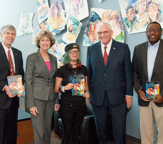 Student holding book poses with dignitaries