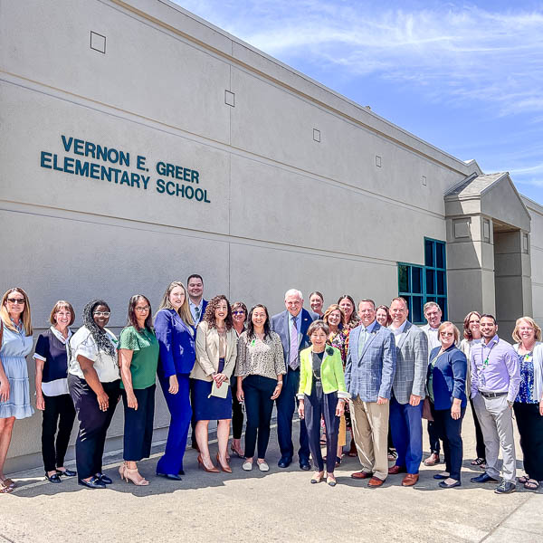 Visitors and school officials posing under Vernon E. Greer Elementary School sign