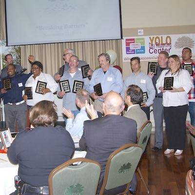 Award recipients holding up plaques while crowd applauds