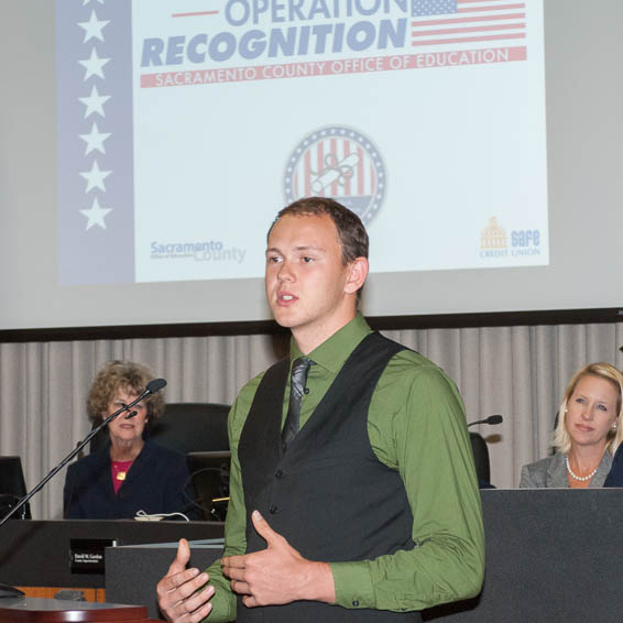 Chase Bowker speaking in front of projected Operation Recognition logo