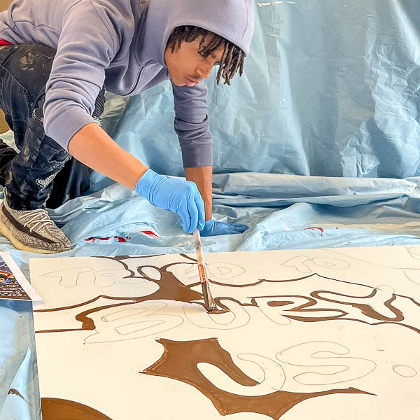 Student painting around outlined 'tried to bury us' text