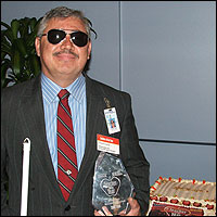 Frank Lopez holding his award, stands next to a Teachers of the Year cake