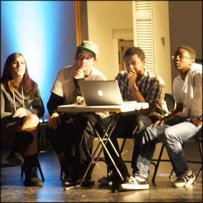Students, seated in front of MacBook, presenting