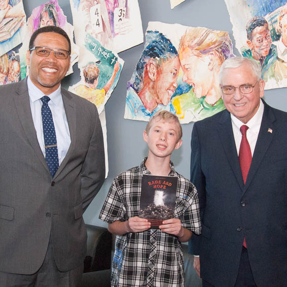 Student holding book stands with dignitaries