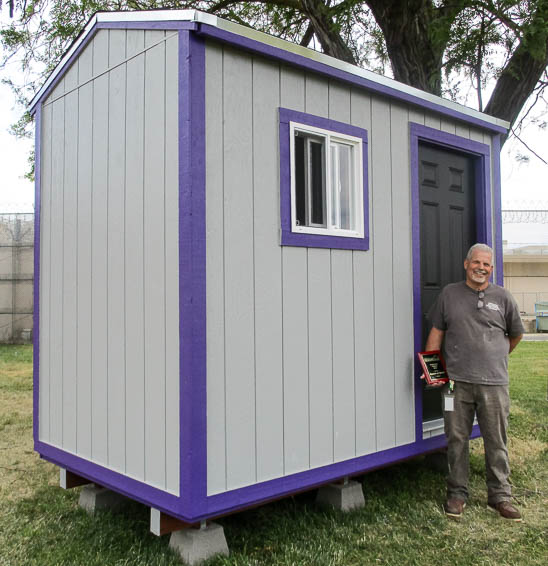 Instructor holding award, posing in front of purple and gray building