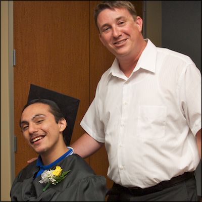 Teacher with smiling student wearing graduation cap and gown